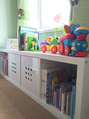 Ikea Kallax storage under the window with books and toys displayed on top