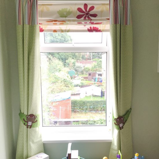 Nursery window with green curtains, monkey tie backs and storage unit underneath